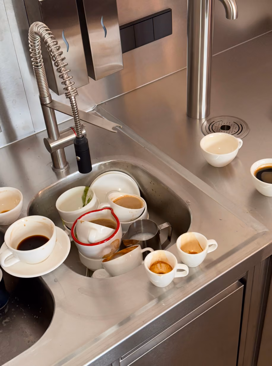 Espresso cups piled in a stainless steel sink at STROM