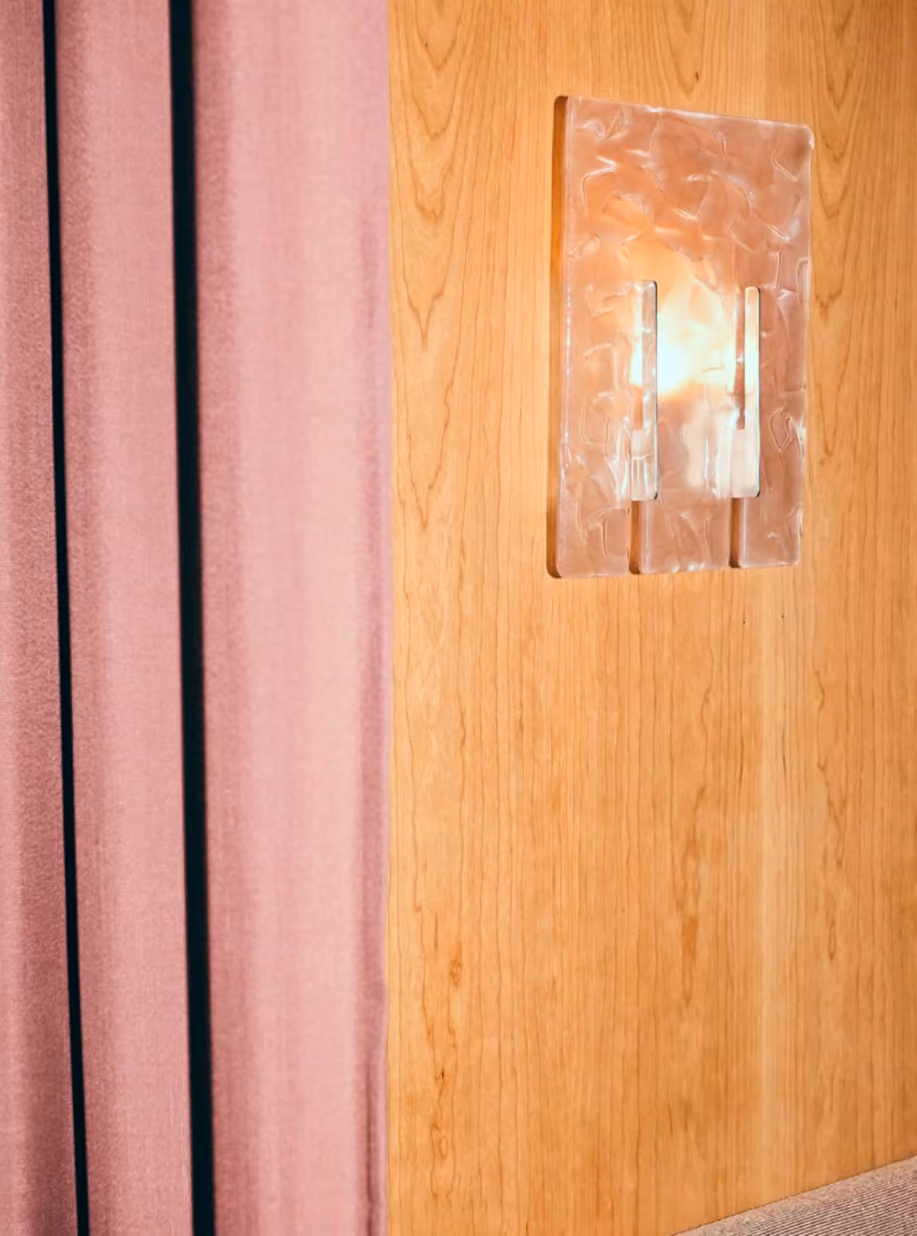 Cast glass wall lamp on wood panelling beside a pink curtain