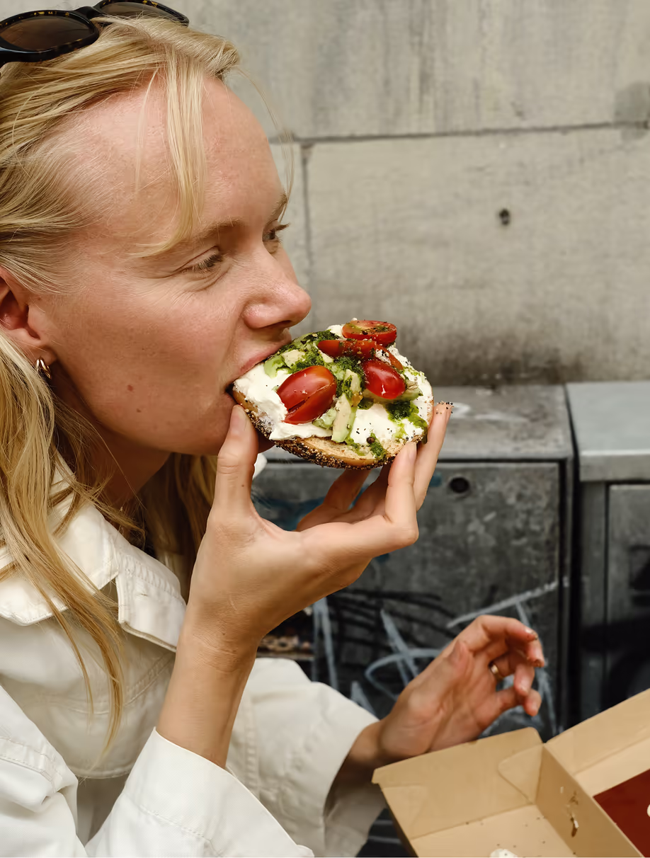 Person biting into a Rolling Bagels bagel on the street