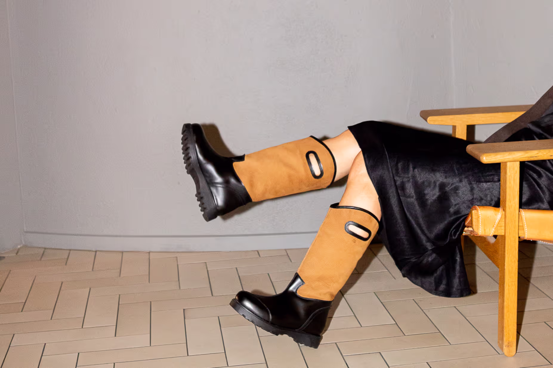 Model in tan and black Blankens boots with her legs resting on a wooden chair
