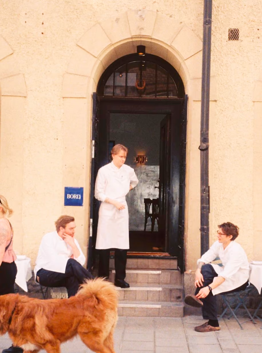 Bord staff relaxing outside the restaurant entrance as a dog walks past