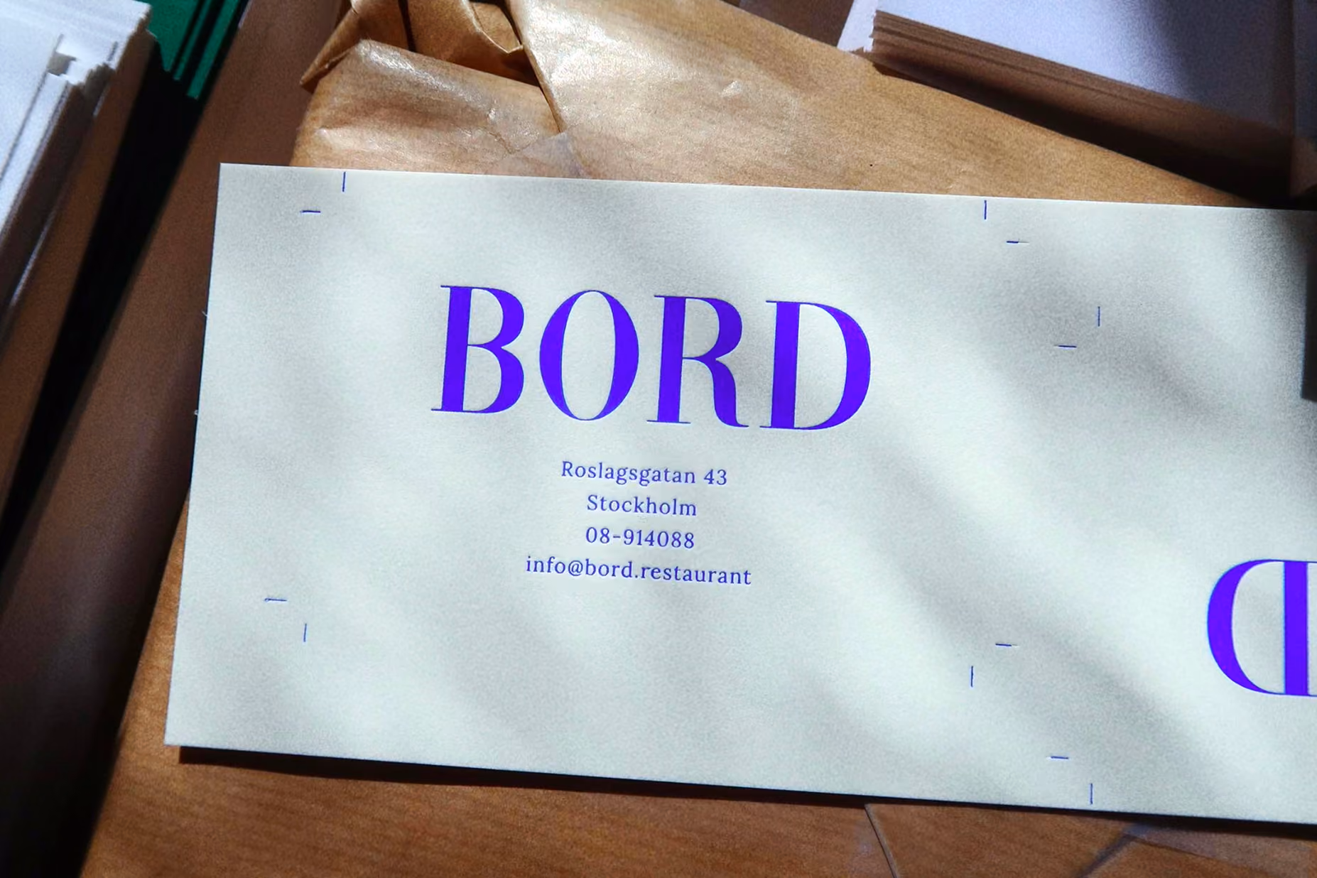 Bord card with the blue logotype, address and contact details, lying on kraft paper