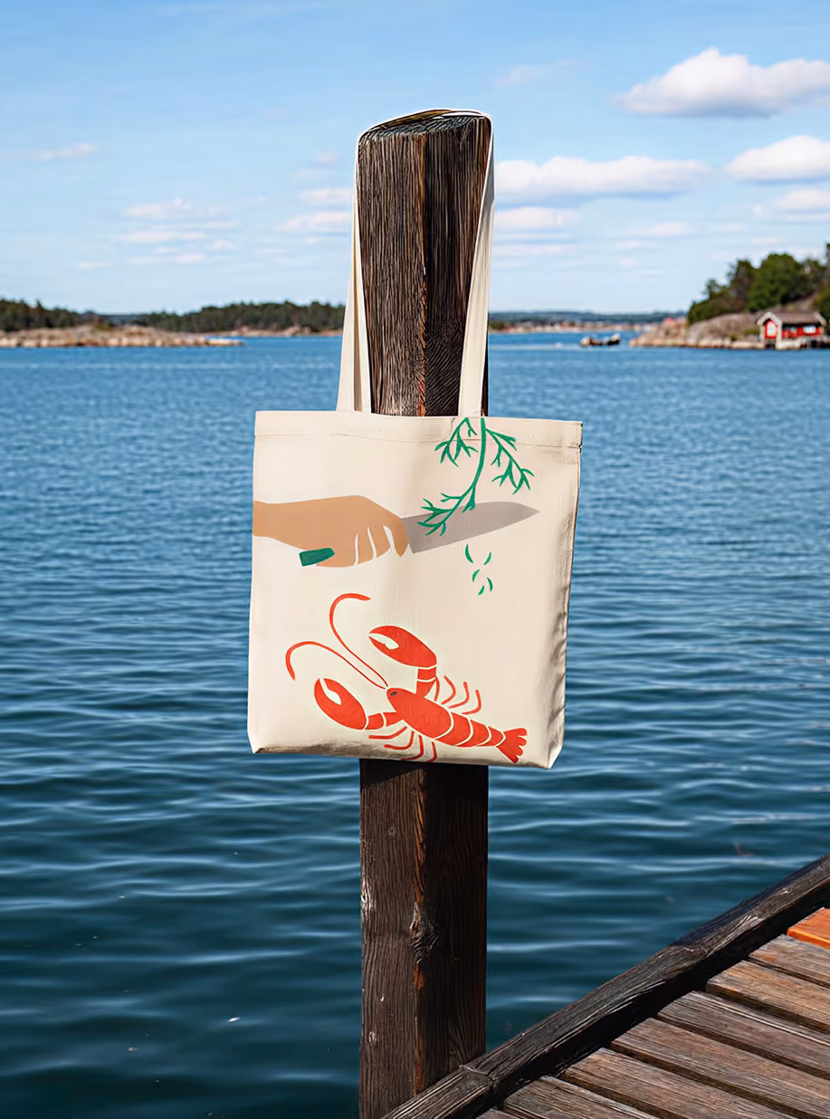 Coop Skärgården tote bag with crayfish illustration hanging on a pier post