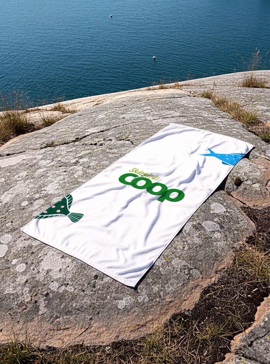 Skärgårds Coop beach towel with fish illustrations spread on coastal rocks