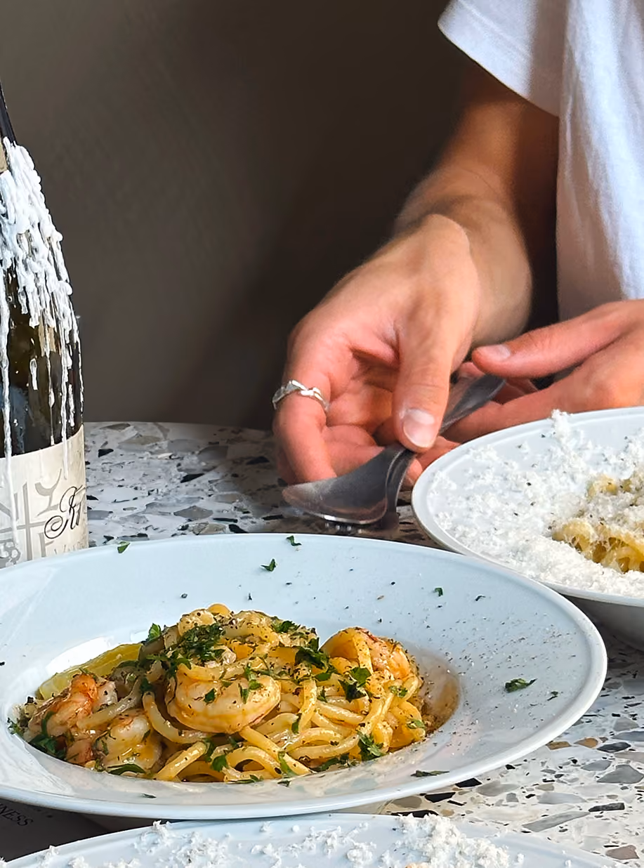 Plates of shrimp pasta and a bottle of wine on a terrazzo table at Cucina Povera