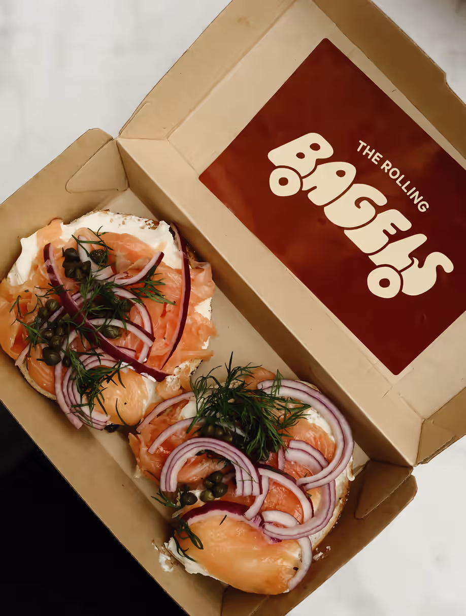 Rolling Bagels takeaway packaging — kraft box with the logotype, holding two salmon bagels