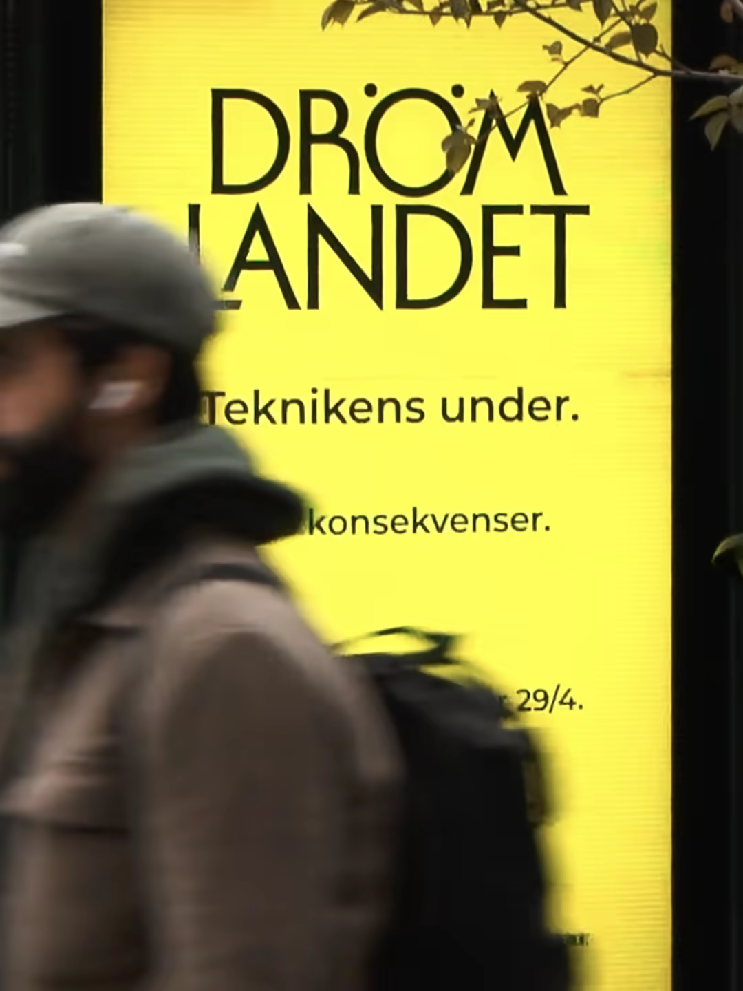 The Drömlandet logotype filling a yellow city board as a commuter walks past